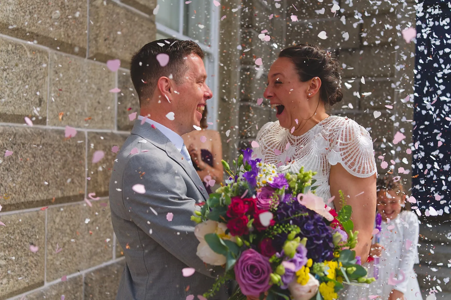 Newlyweds laughing beneath colourful confetti outside their Cornwall wedding