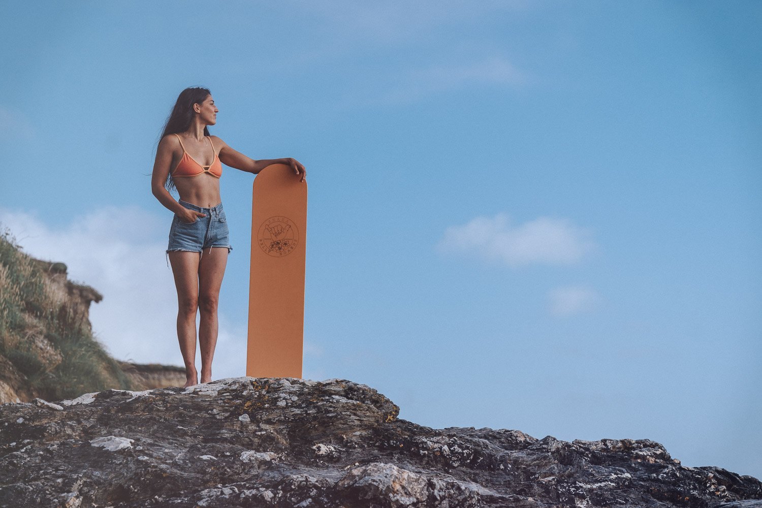 Brand shoot on a Cornish clifftop: woman standing beside a wooden paddleboard above the sea, commercial photography by Lee Searle
