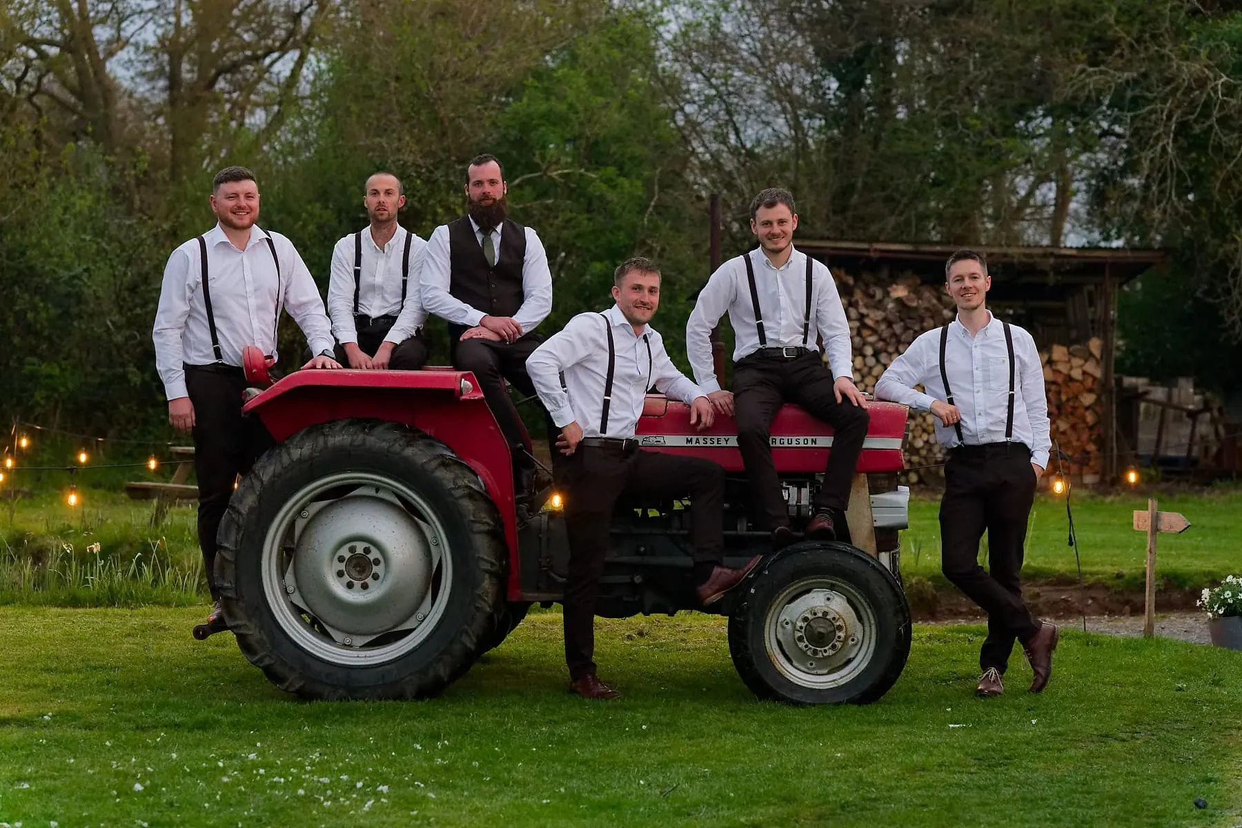 Groom and groomsmen gathered around a red tractor at a Cornwall farm wedding
