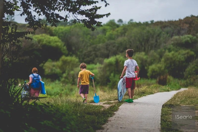 Children walking ahead with buckets and spades along a Cornish coast path on the way to the beach