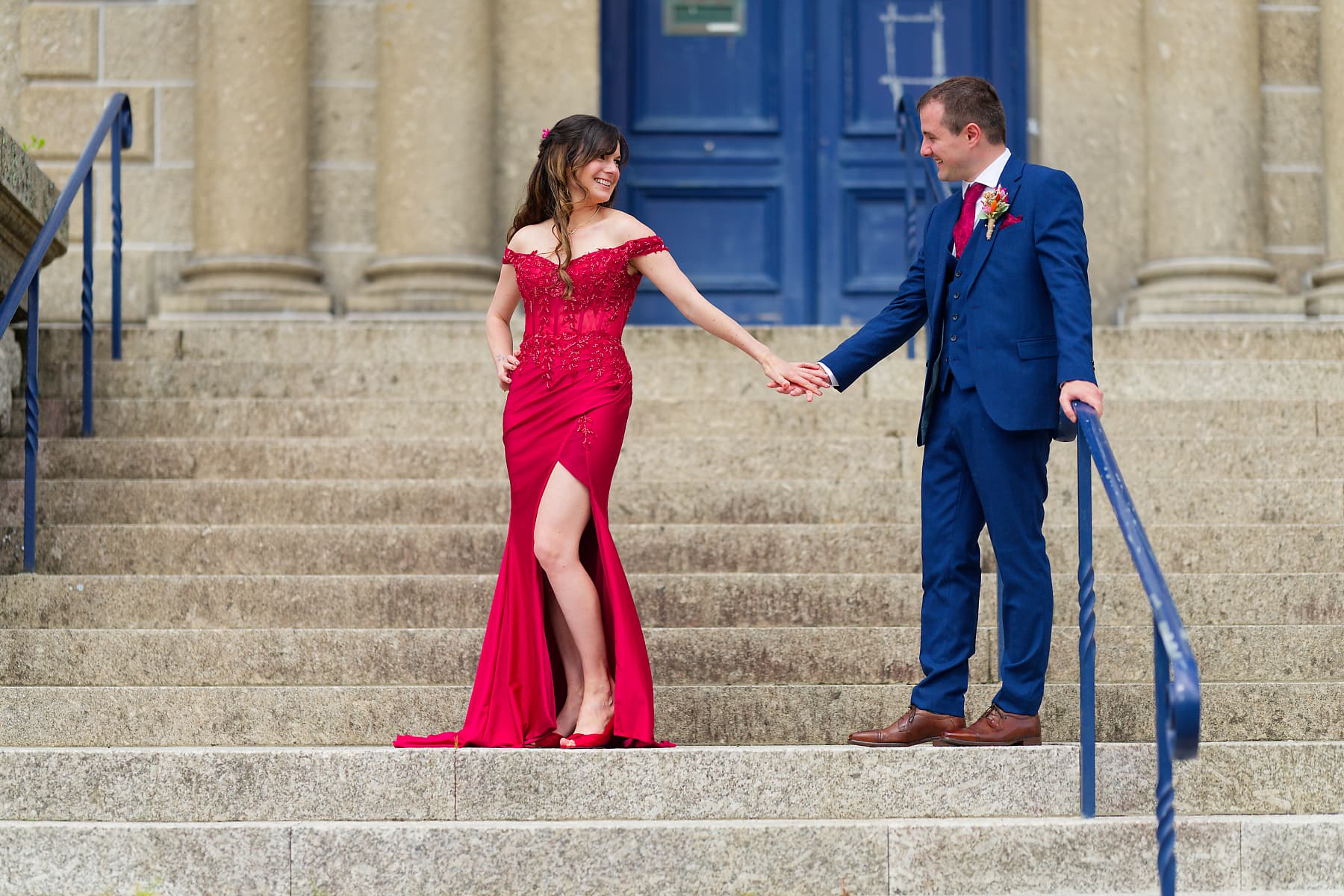 Bride in red and groom in blue on stone steps at a Cornwall wedding venue