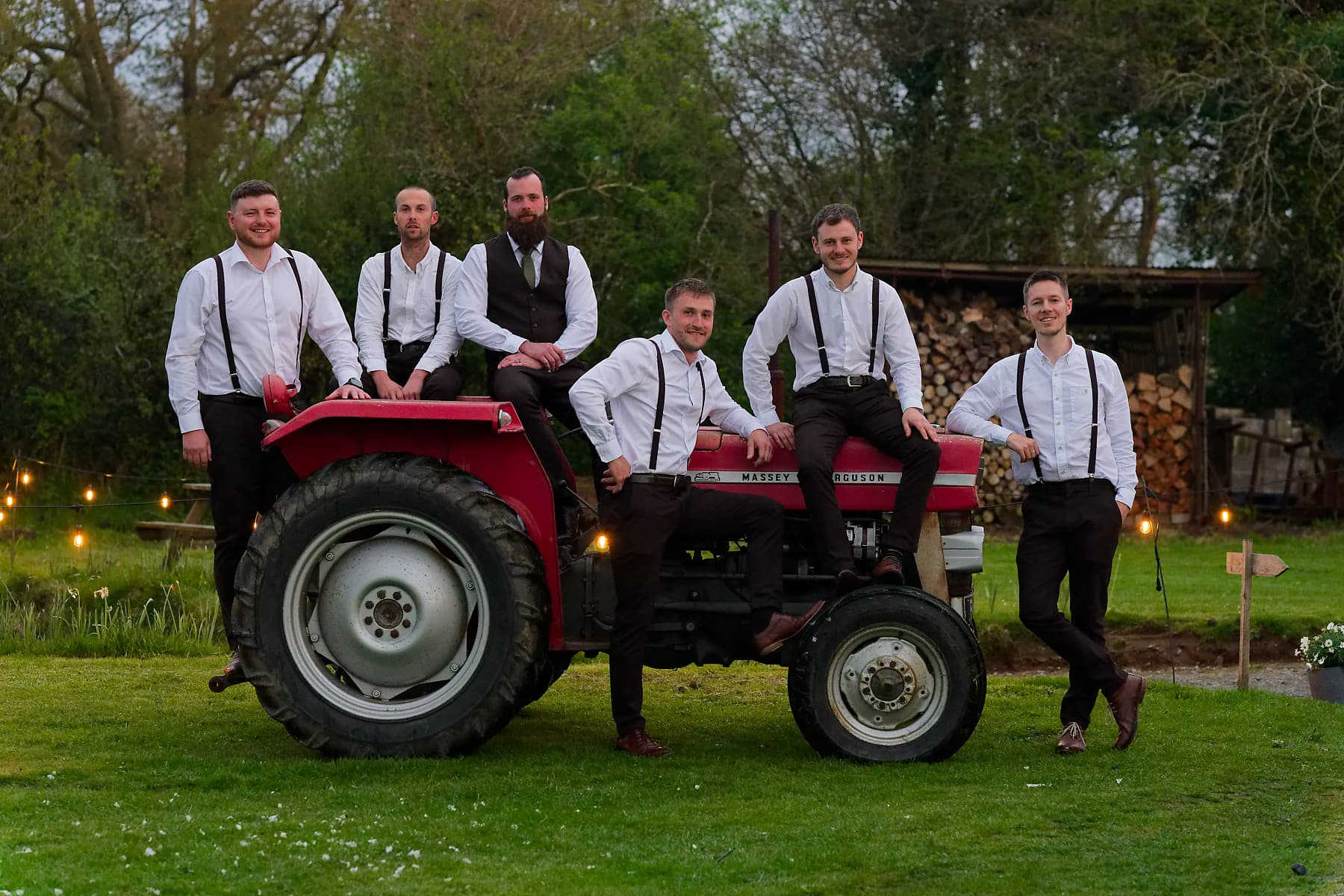 Groom and groomsmen around a red tractor at a Cornwall farm wedding