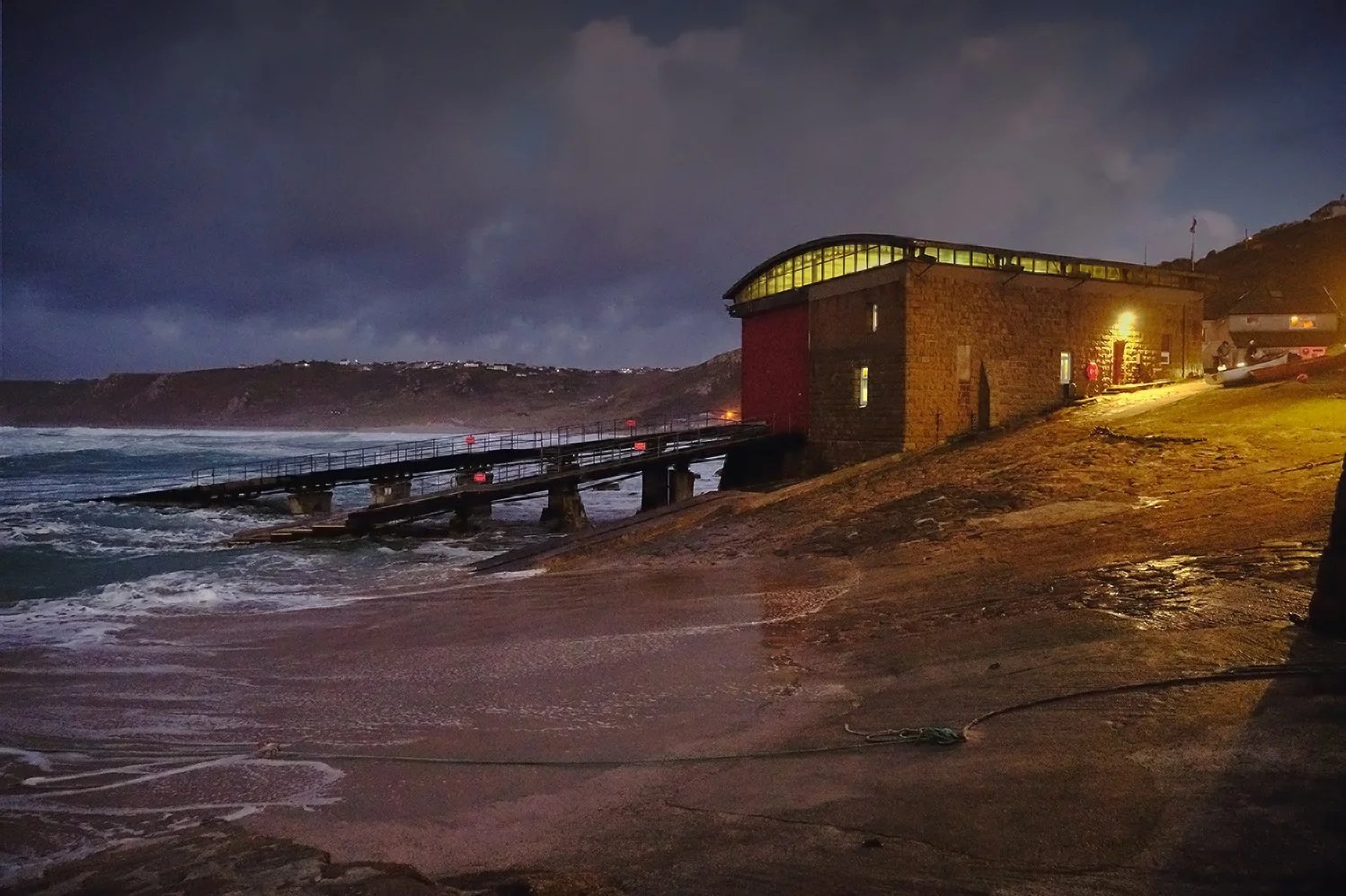 Lifeboat station lit up at dusk above a stormy Cornish sea