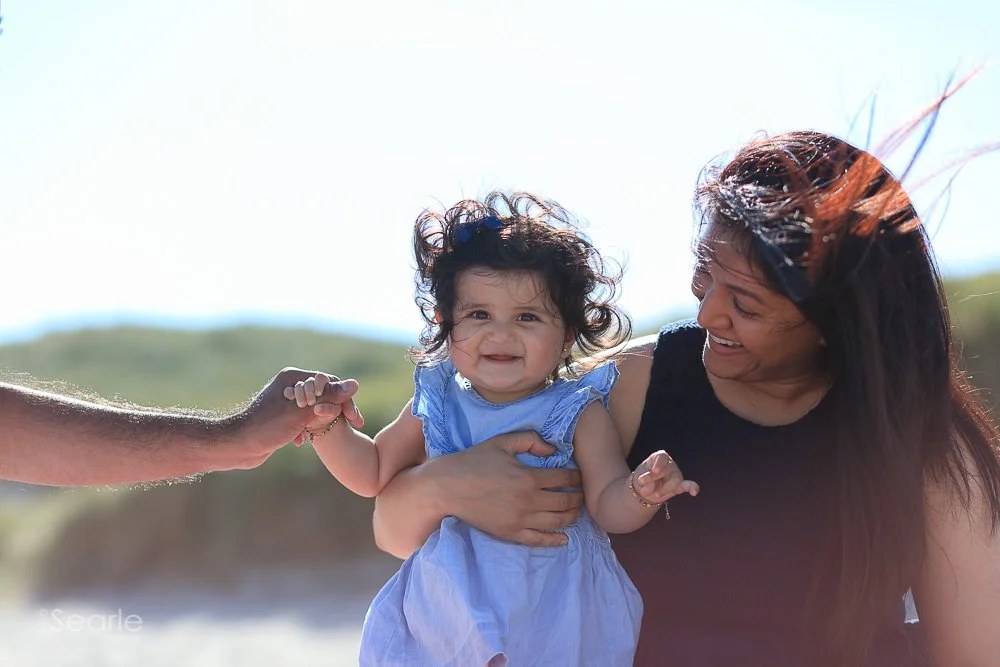 Relaxed family photography in Cornwall: mother holding her baby daughter in the dunes while dad holds her hand