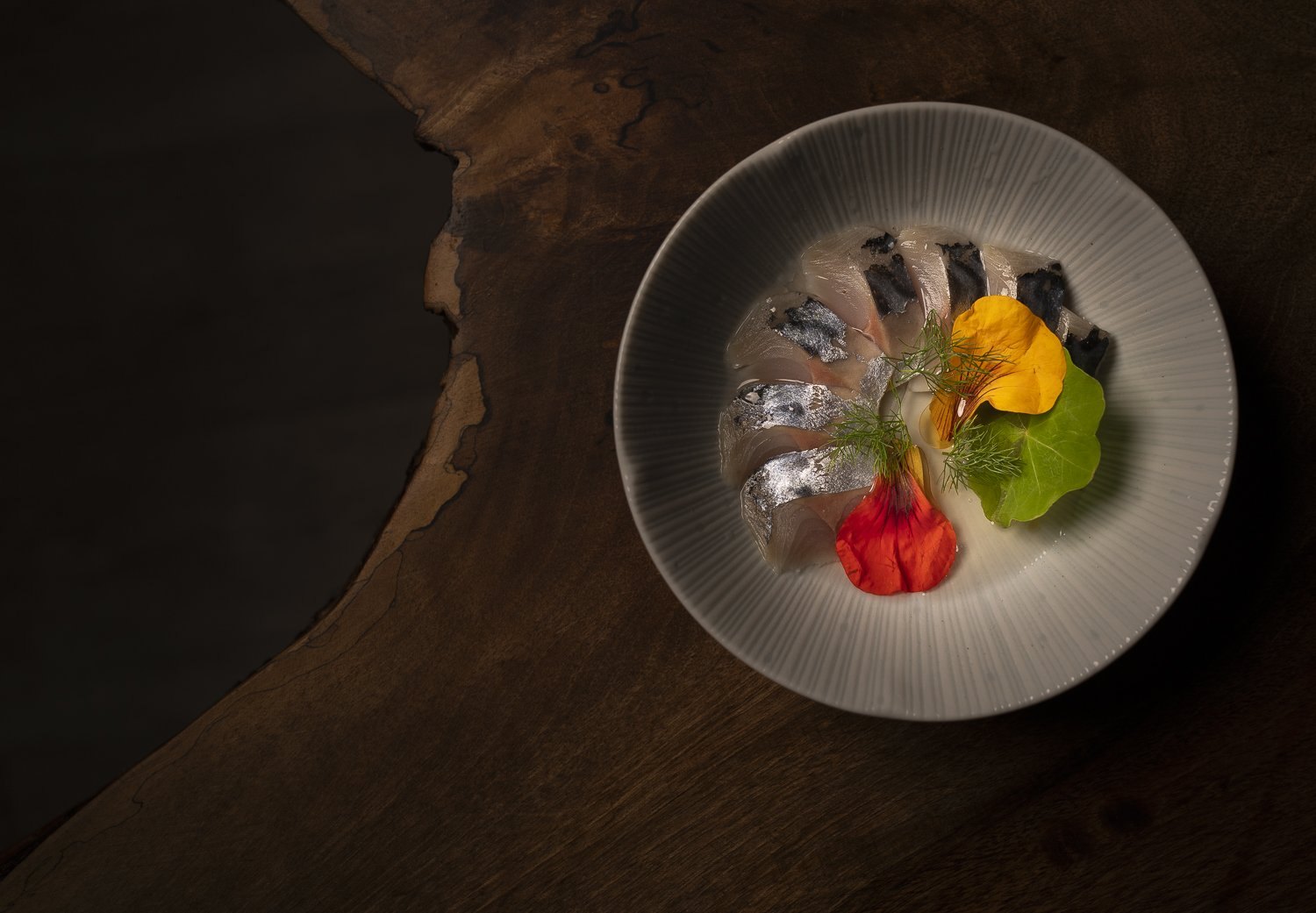 Delicate tasting-menu plate shot from above on dark wood, Penzance restaurant photography