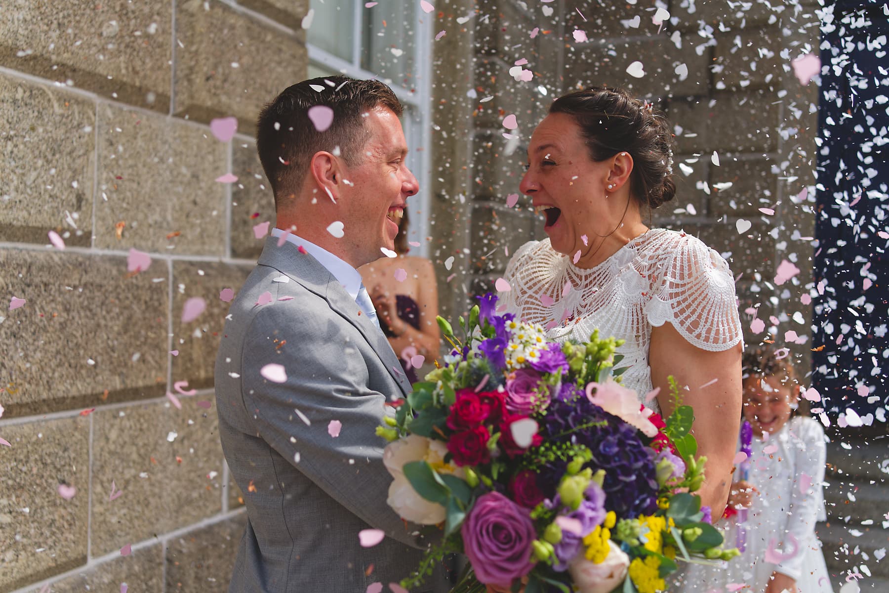 Newlyweds laughing beneath a confetti shower at their Cornwall wedding