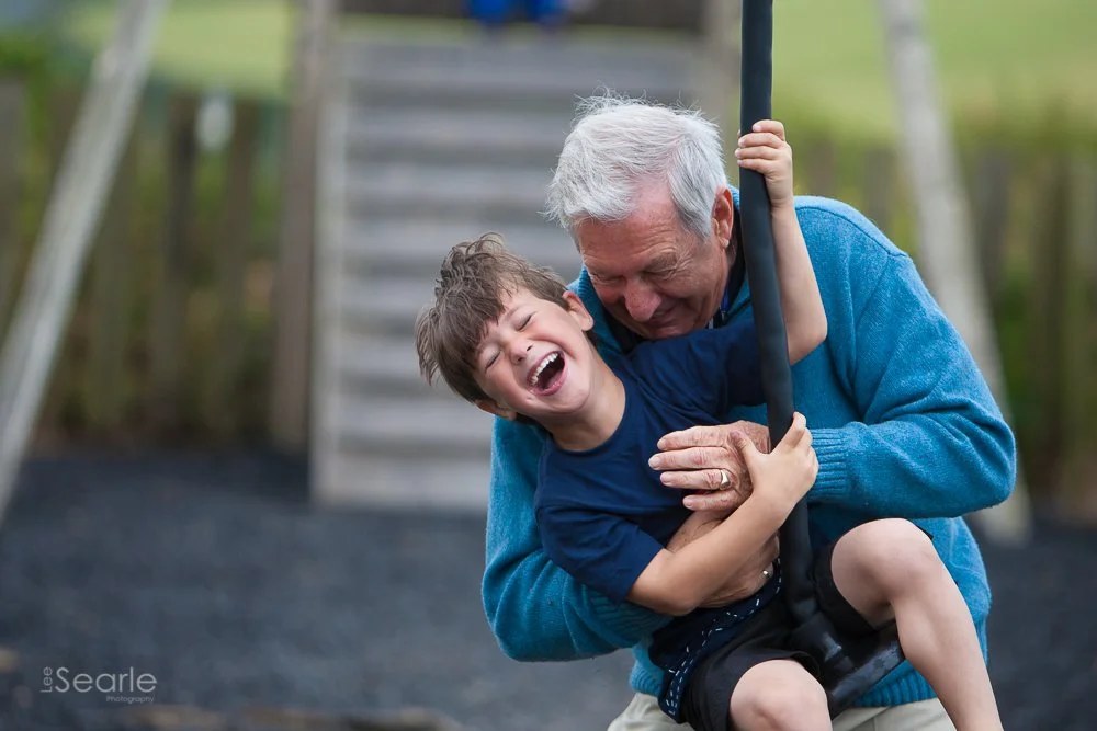 Grandfather swinging his laughing grandson in a Cornish garden during a relaxed family photo session