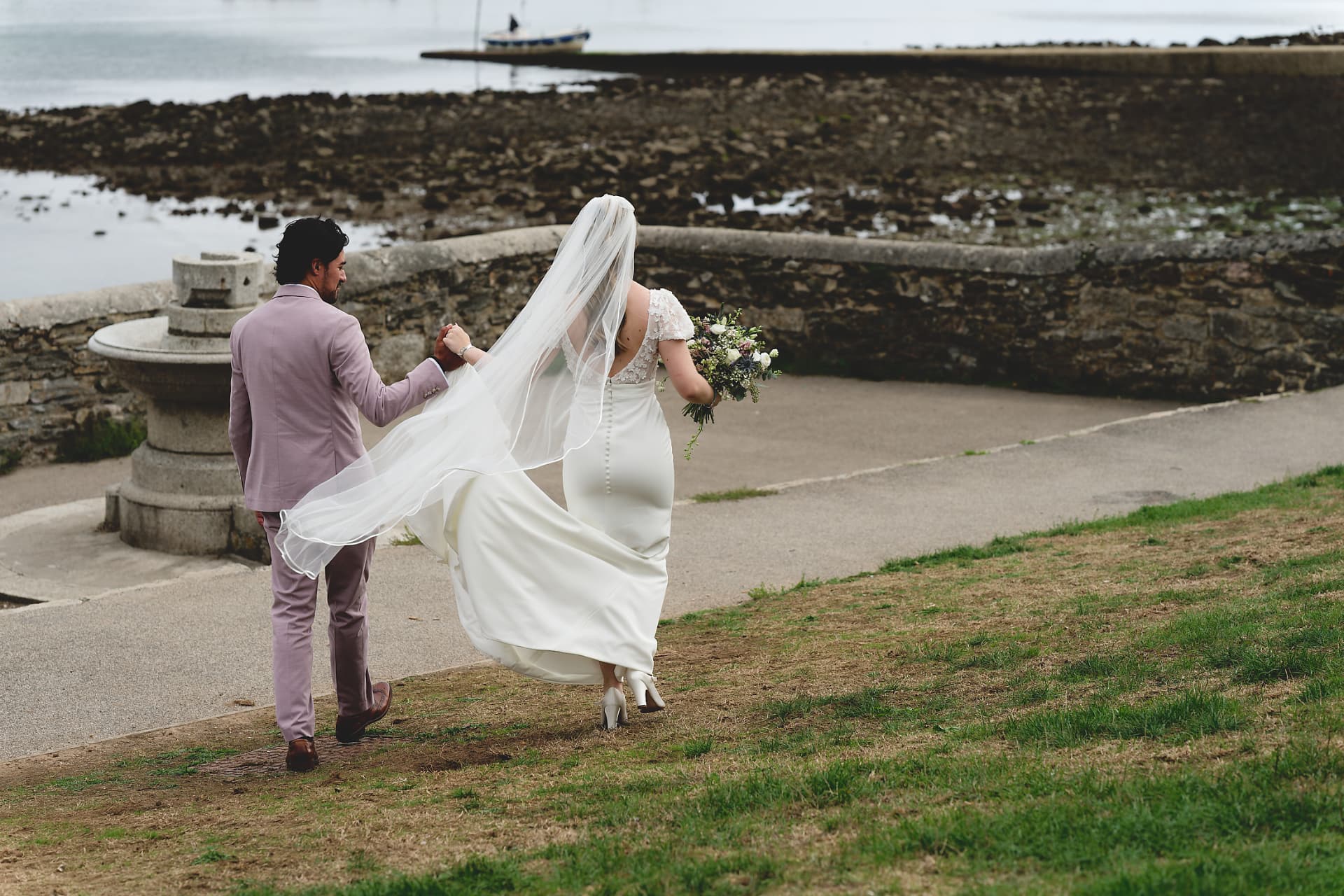 Cornwall elopement couple on the coast path Couple walking hand in hand along a Cornwall coastal path after their elopement
